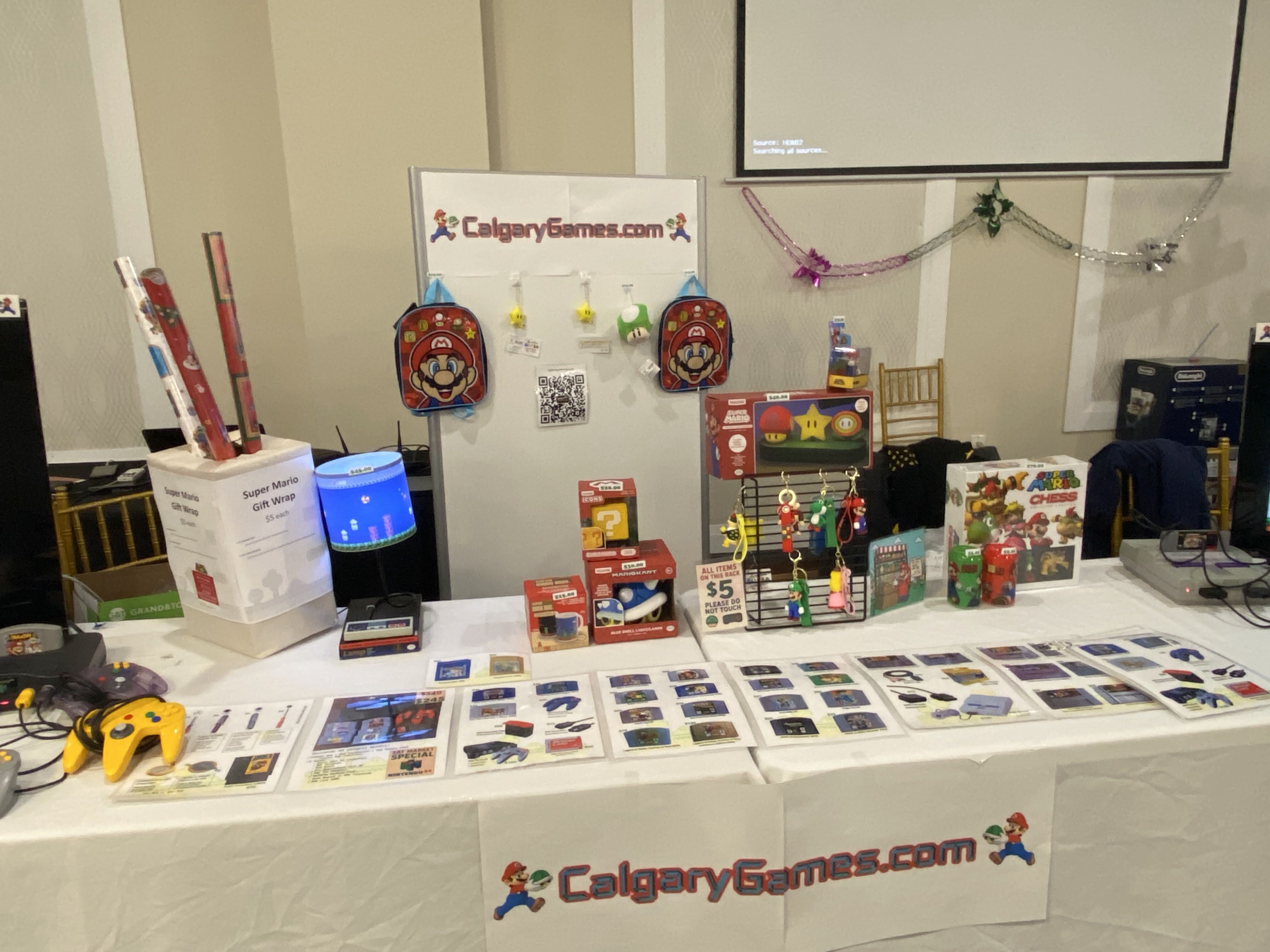 Calgary Games booth close-up showing Mario merchandise, Bitcoin collectibles, and console reference sheets